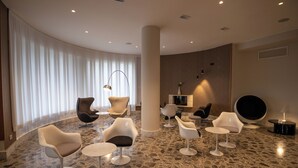 Uma área de estar moderna com cadeiras contemporâneas, uma mesa redonda e uma janela grande com cortinas leves.