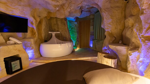 Um quarto de spa com uma banheira grande, um banco de madeira e uma televisão na parede.