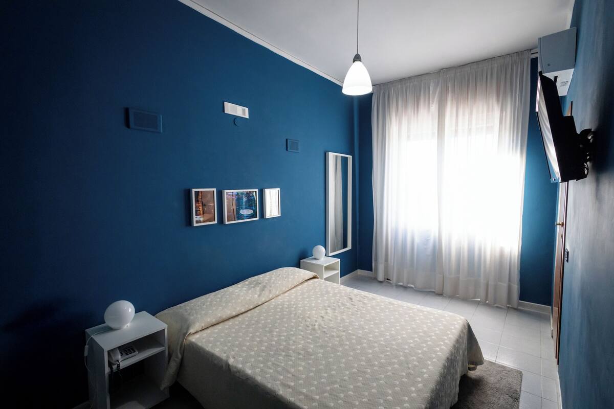A bedroom with a bed, bedside tables, a mirror, and a window with curtains.