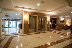 A hotel lobby with a marble floor, two elevators, a reception desk, and a seating area. - Taksim Metropark Hotel (Istanbul)