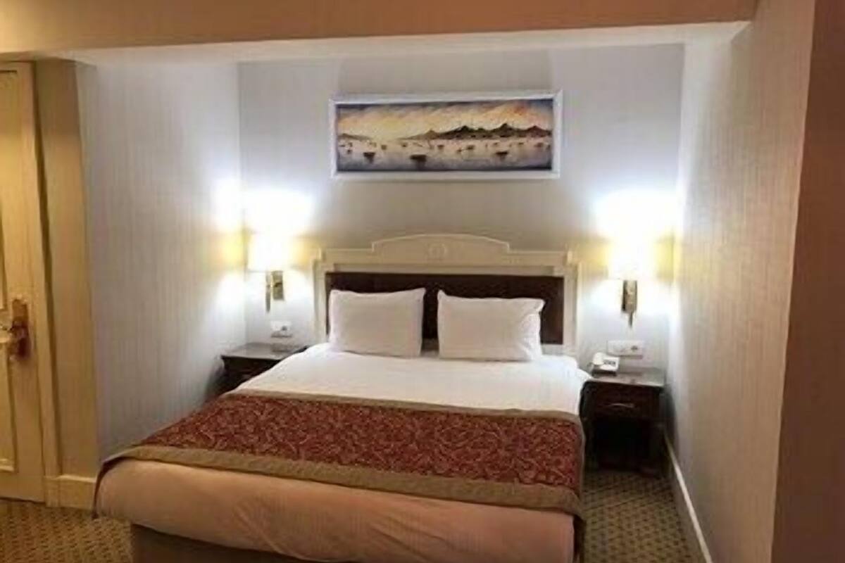 A hotel room with a bed, a painting on the wall, and two bedside lamps.