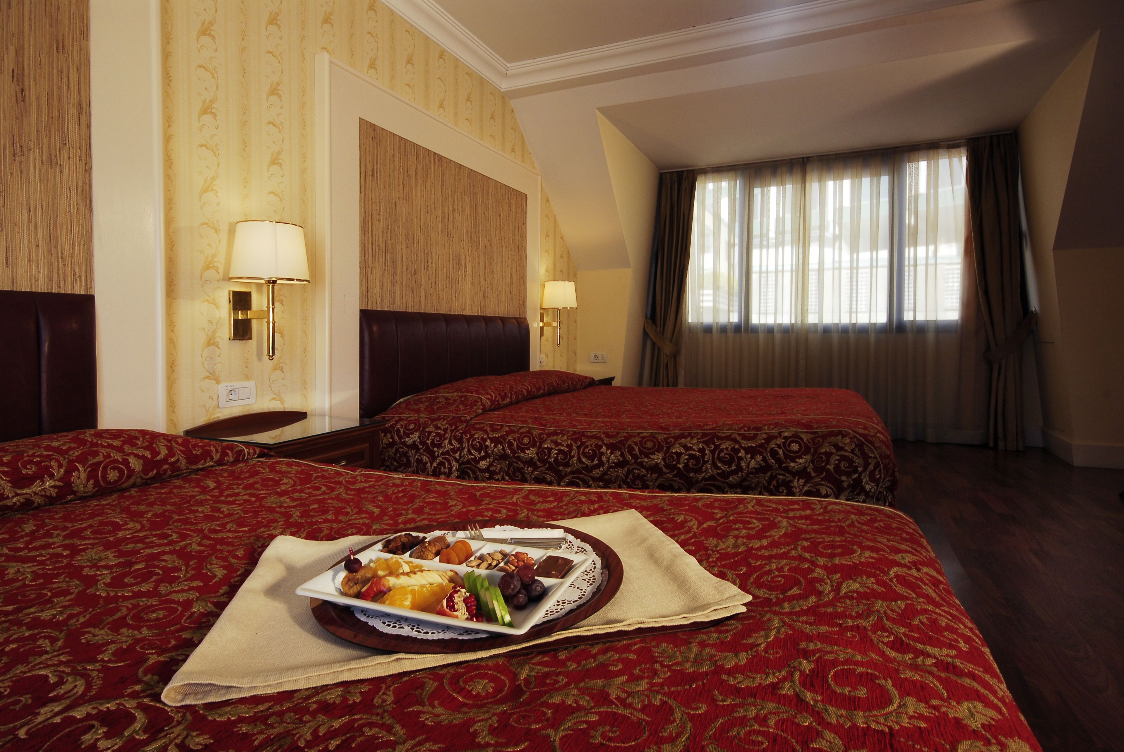 A hotel room with two beds, a dining table with a plate of food, and a window with curtains.