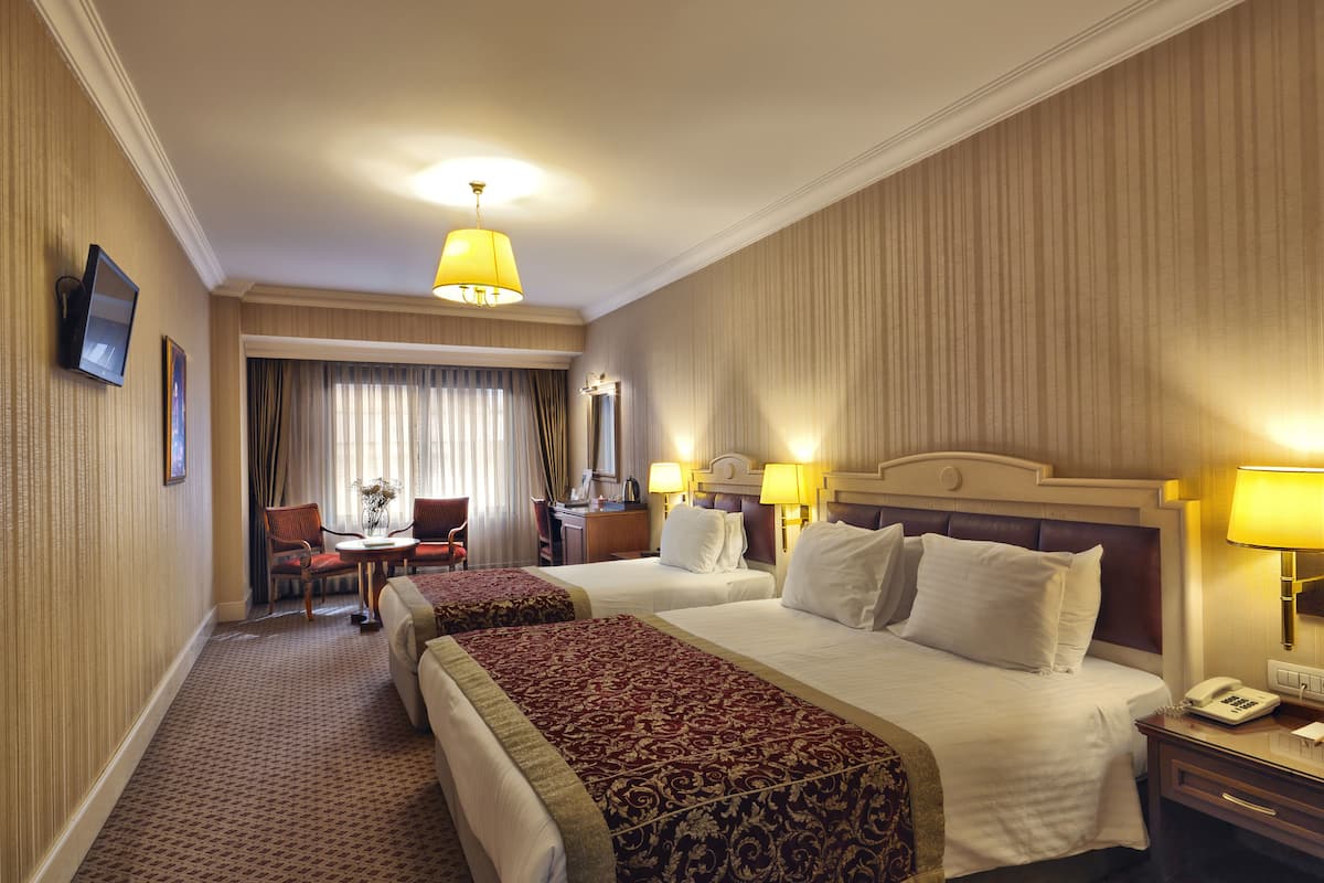A hotel room with two beds, a desk, a chair, and a TV.