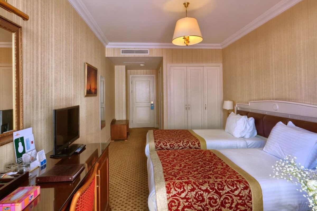 A hotel room with a large bed, a smaller bed, a desk with a TV, a mirror, and a wardrobe.