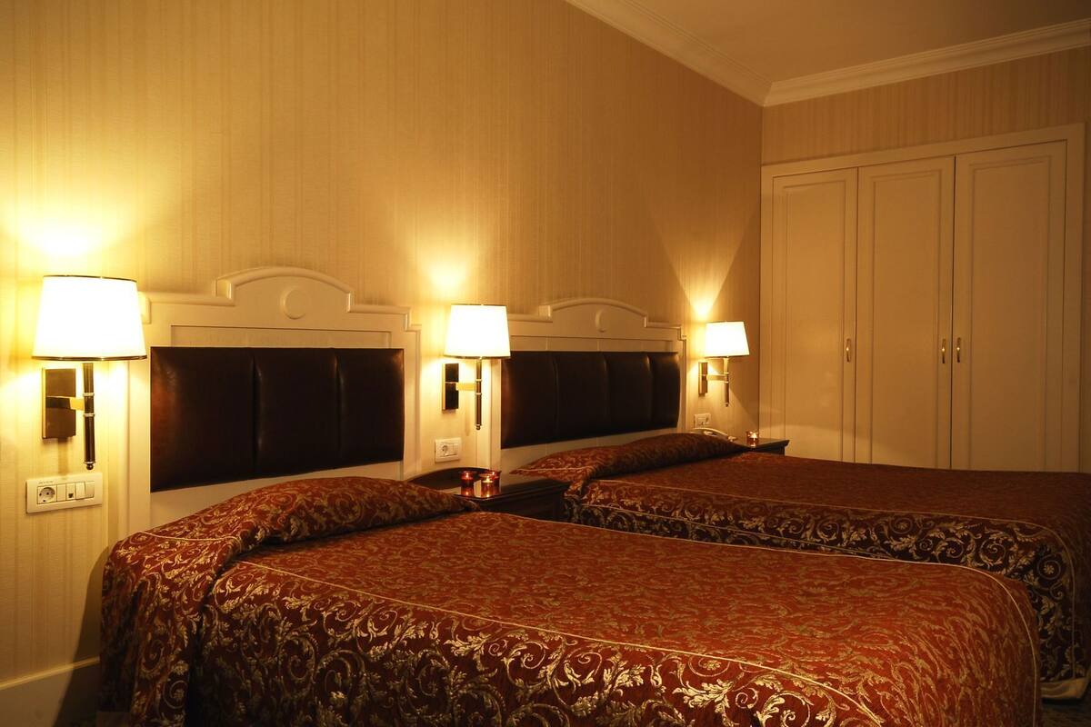 A hotel room with two beds, headboards, bedside lamps, a nightstand, and a wardrobe.