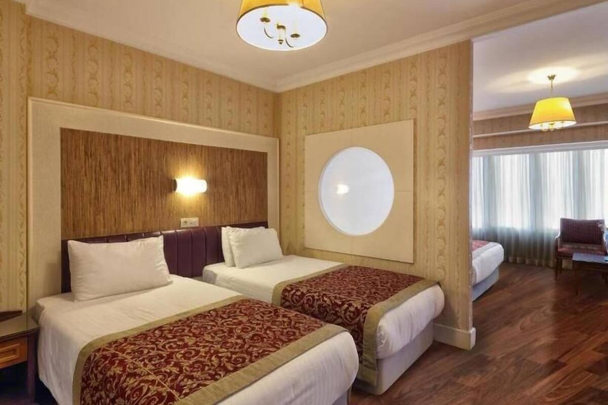A hotel room with two beds, a large mirror, a round wall clock, and a view of the outdoors through the window.