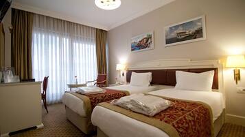 A hotel room with two beds, a desk, a chair, and a window with curtains.