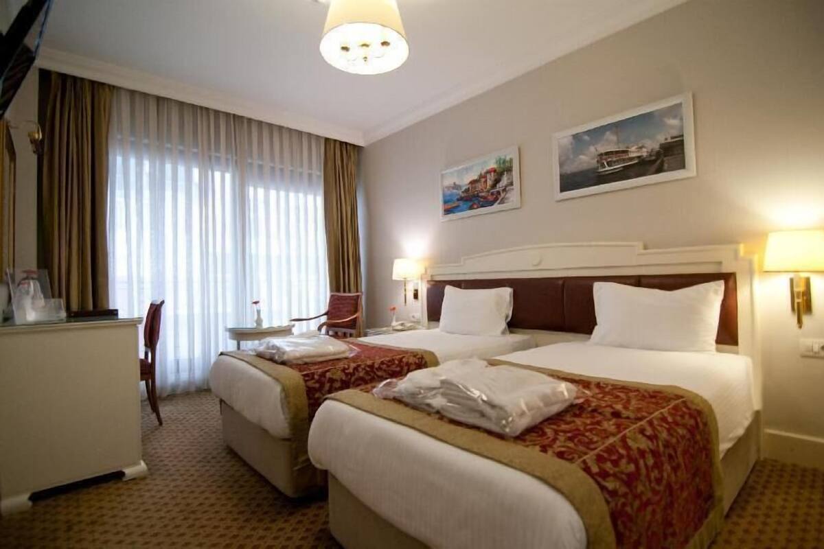 A hotel room with two beds, a desk, a chair, and a window with curtains.