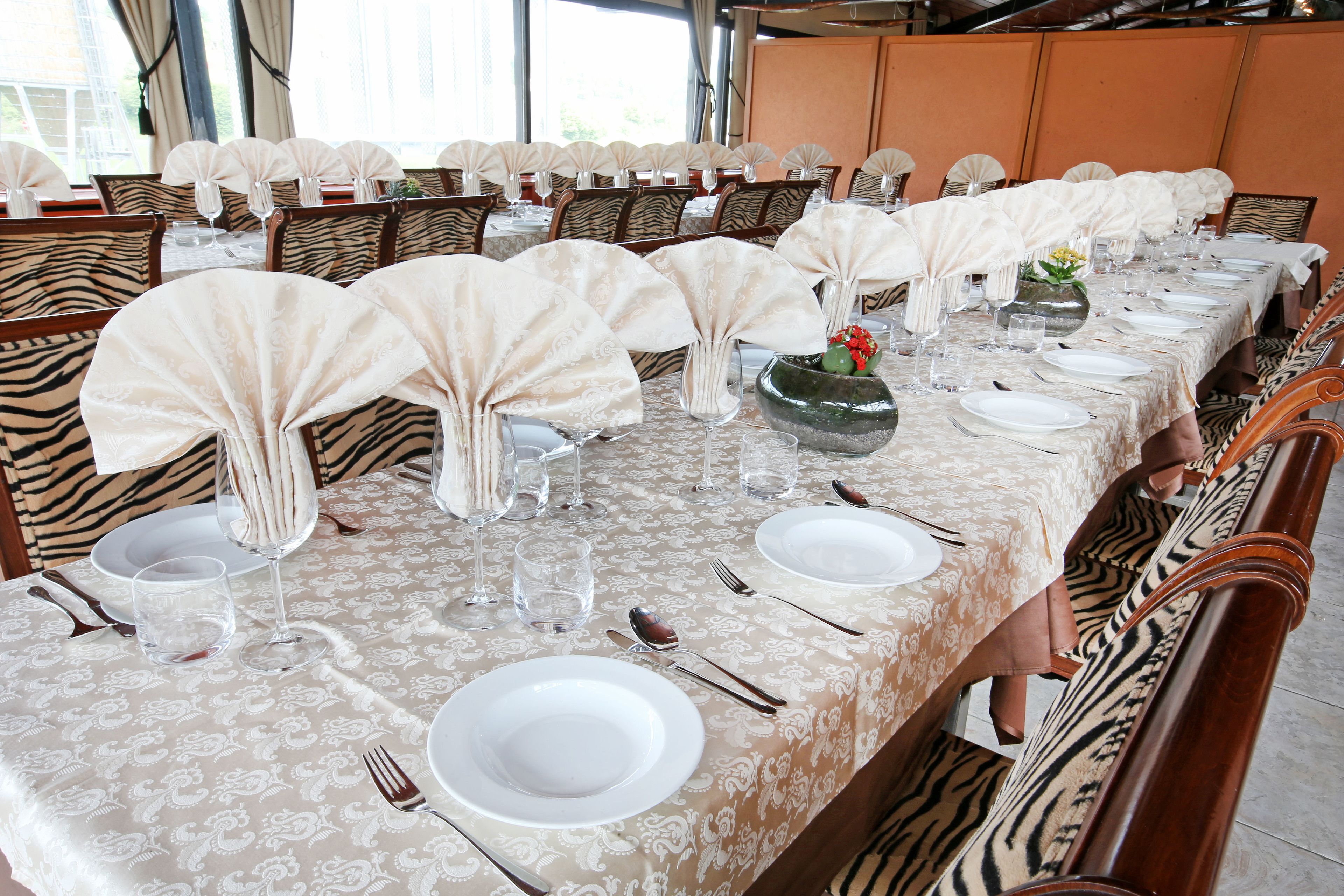 Une table à manger dressée avec de l’argenterie blanche, des couverts et des verres, entourée de chaises à rayures zébrées.