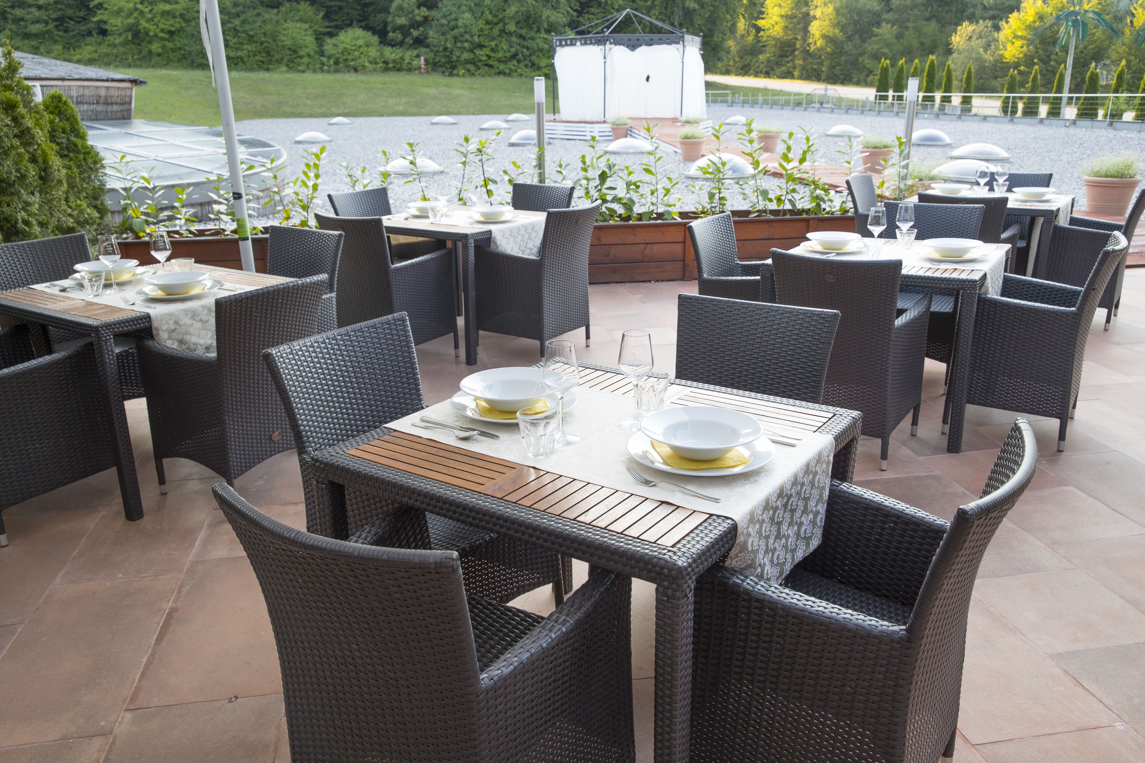 Un espace extérieur aménagé pour les repas, avec des tables et des chaises en osier, disposées sur une terrasse carrelée.