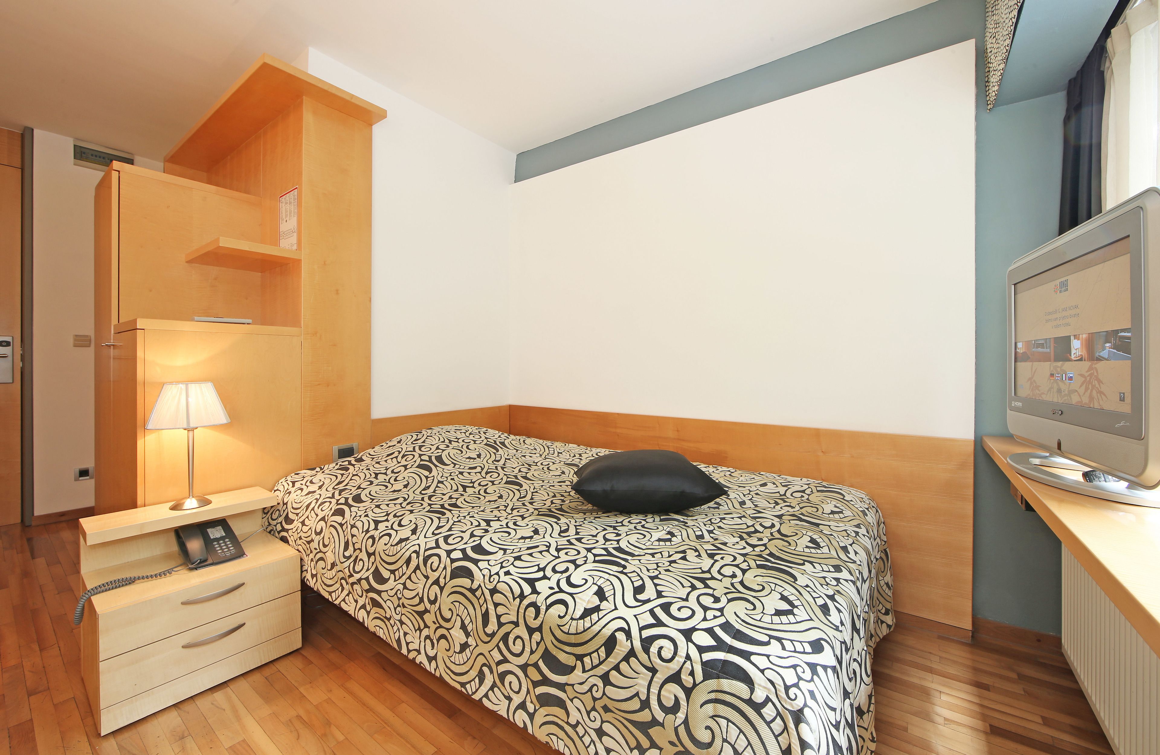 Une chambre à coucher avec une couvre-lit à motifs, une lampe de chevet, une armoire en bois et un téléviseur posé sur un meuble.