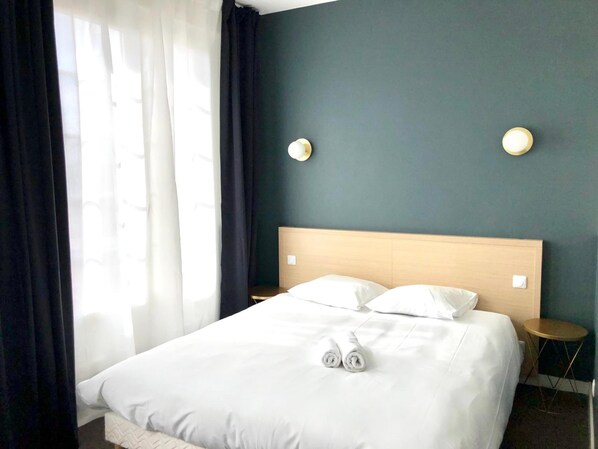 A hotel room with a large bed, two bedside tables, and a window with curtains. - Saint-Louis (Brest)