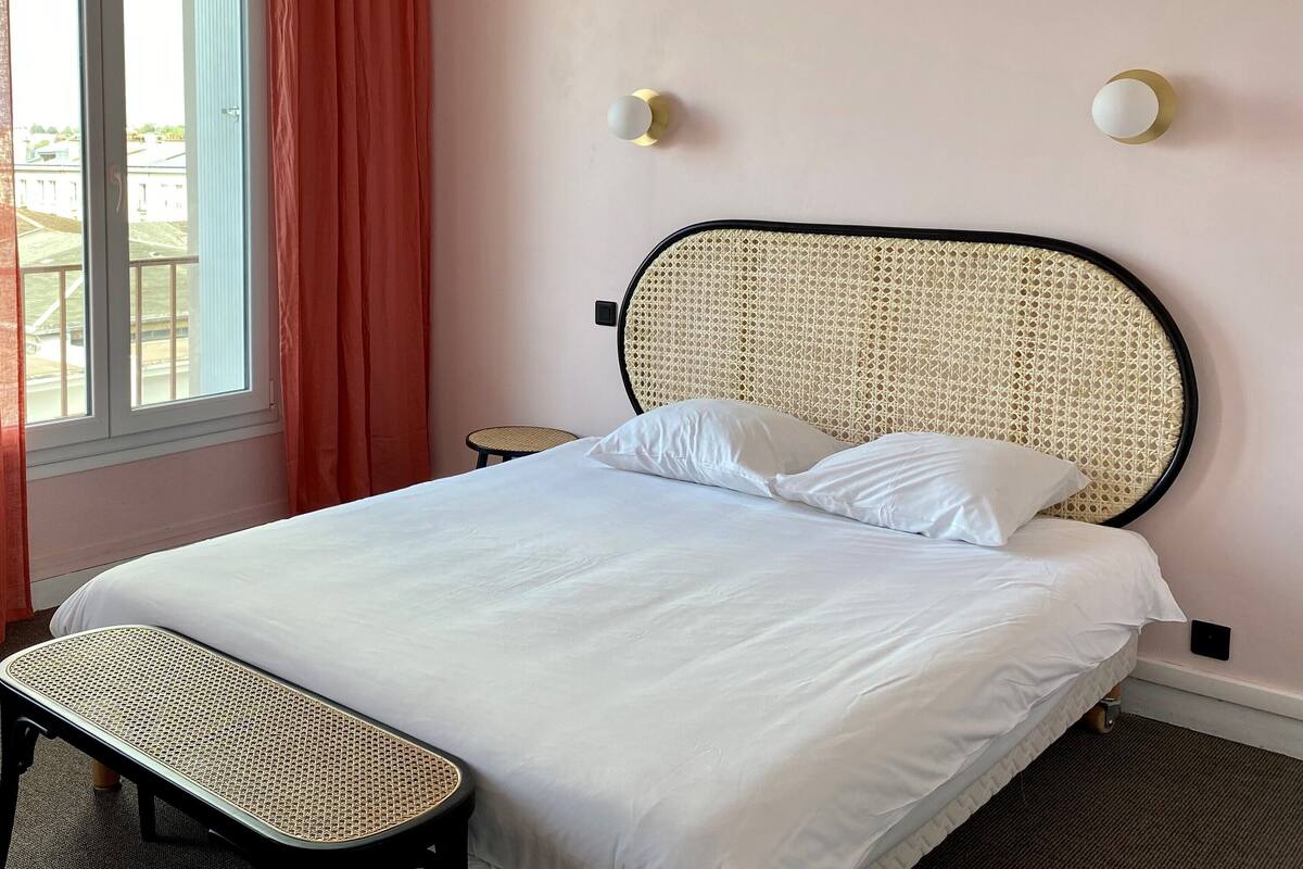 A neatly made bed with white linens, a wicker headboard, and a small bedside table.