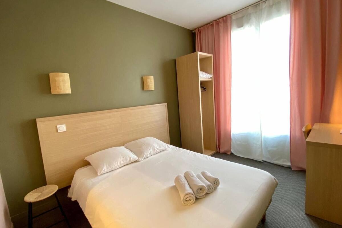 A hotel room with a large bed, a small stool, a wardrobe, and a window with curtains.