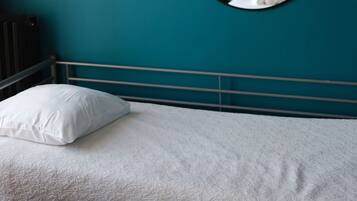 A bed with a white pillow and a textured blanket, a round mirror on the wall, and a teal-colored wall.