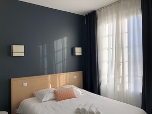 A hotel room with a bed, a nightstand, and a window with curtains. - Saint-Louis (Brest)
