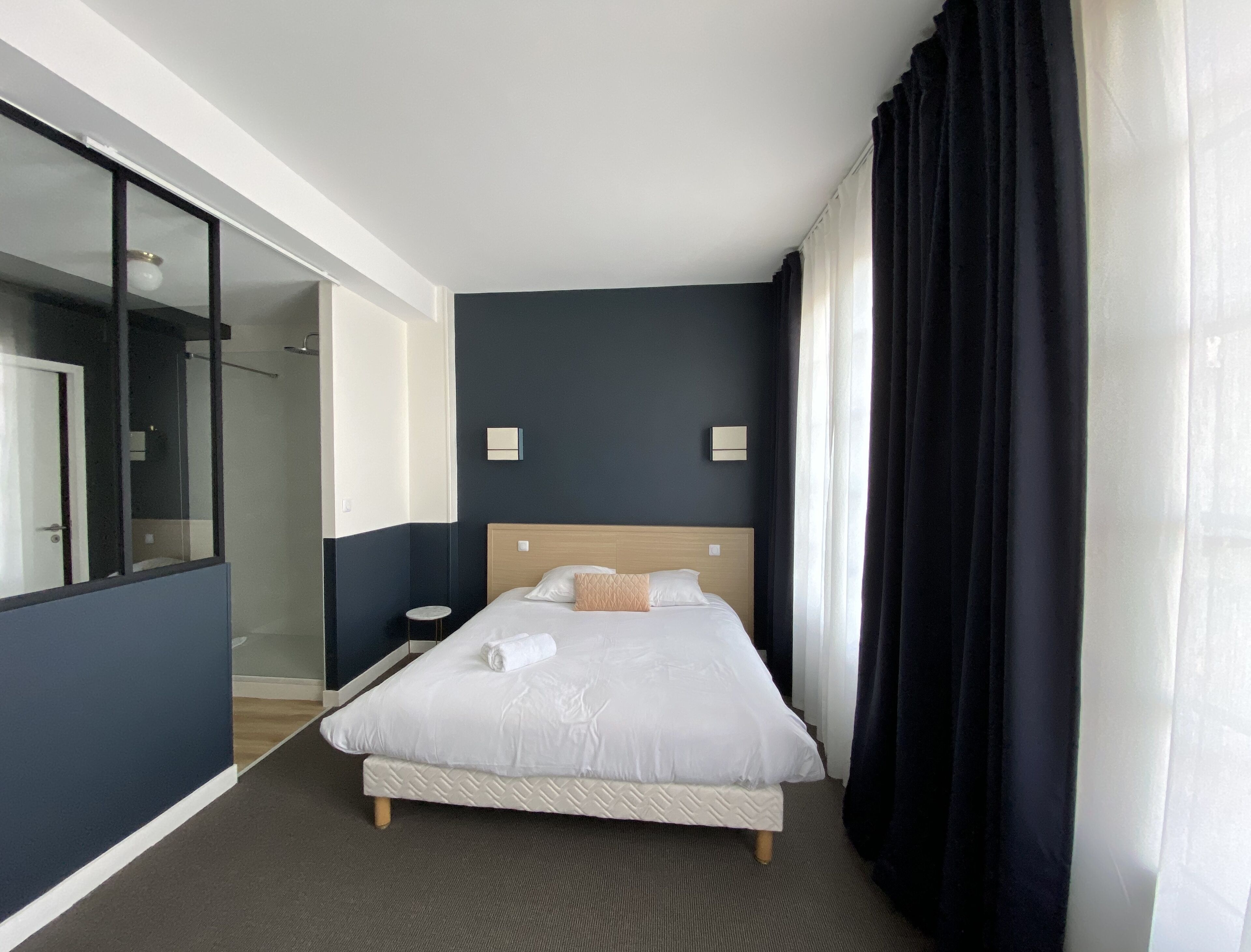 Habitación de hotel con una cama grande, una mesita de noche, un espejo y vistas a un pasillo.