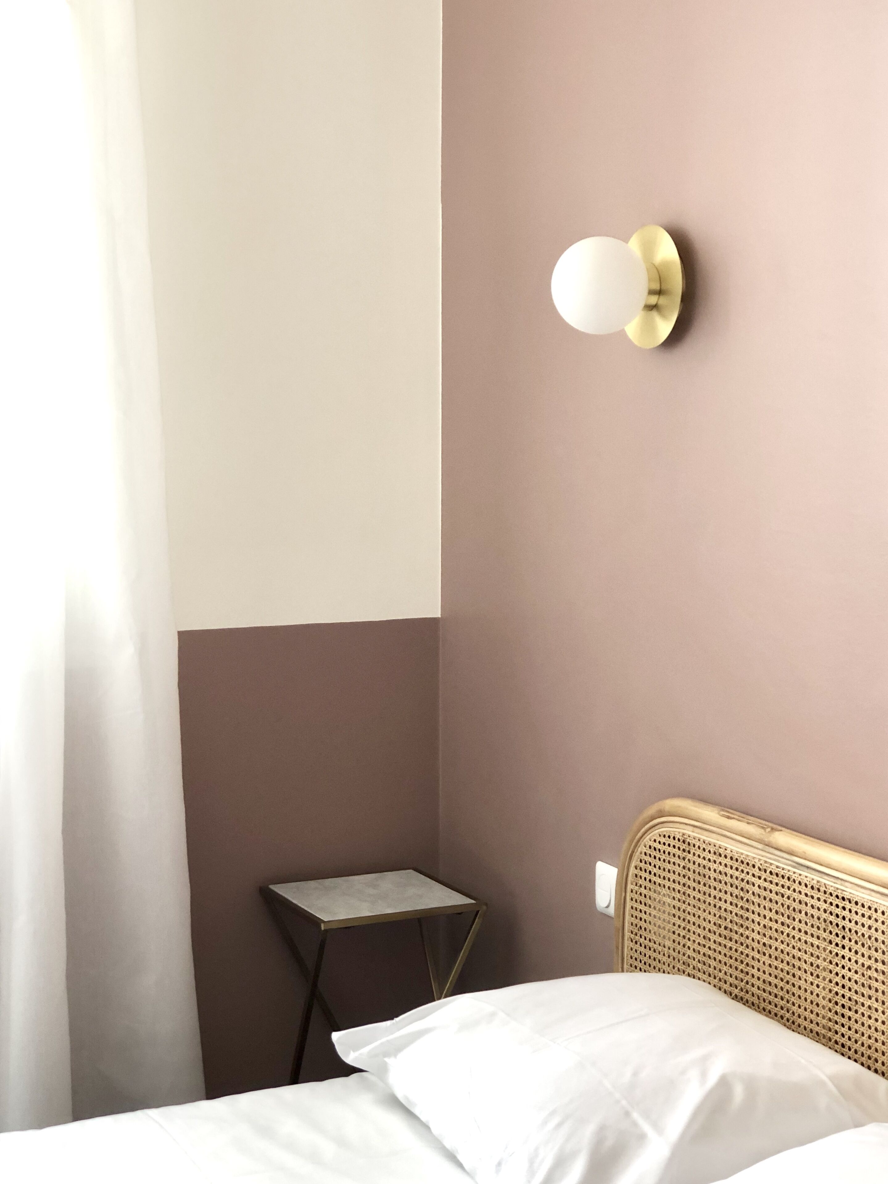 A hotel room with a bed, a small table, and a wall-mounted light fixture.
