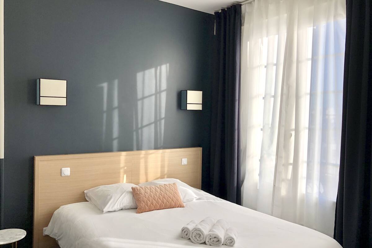 A neatly made bed with white linens and a single decorative pillow, a bedside table, and two wall-mounted light fixtures.