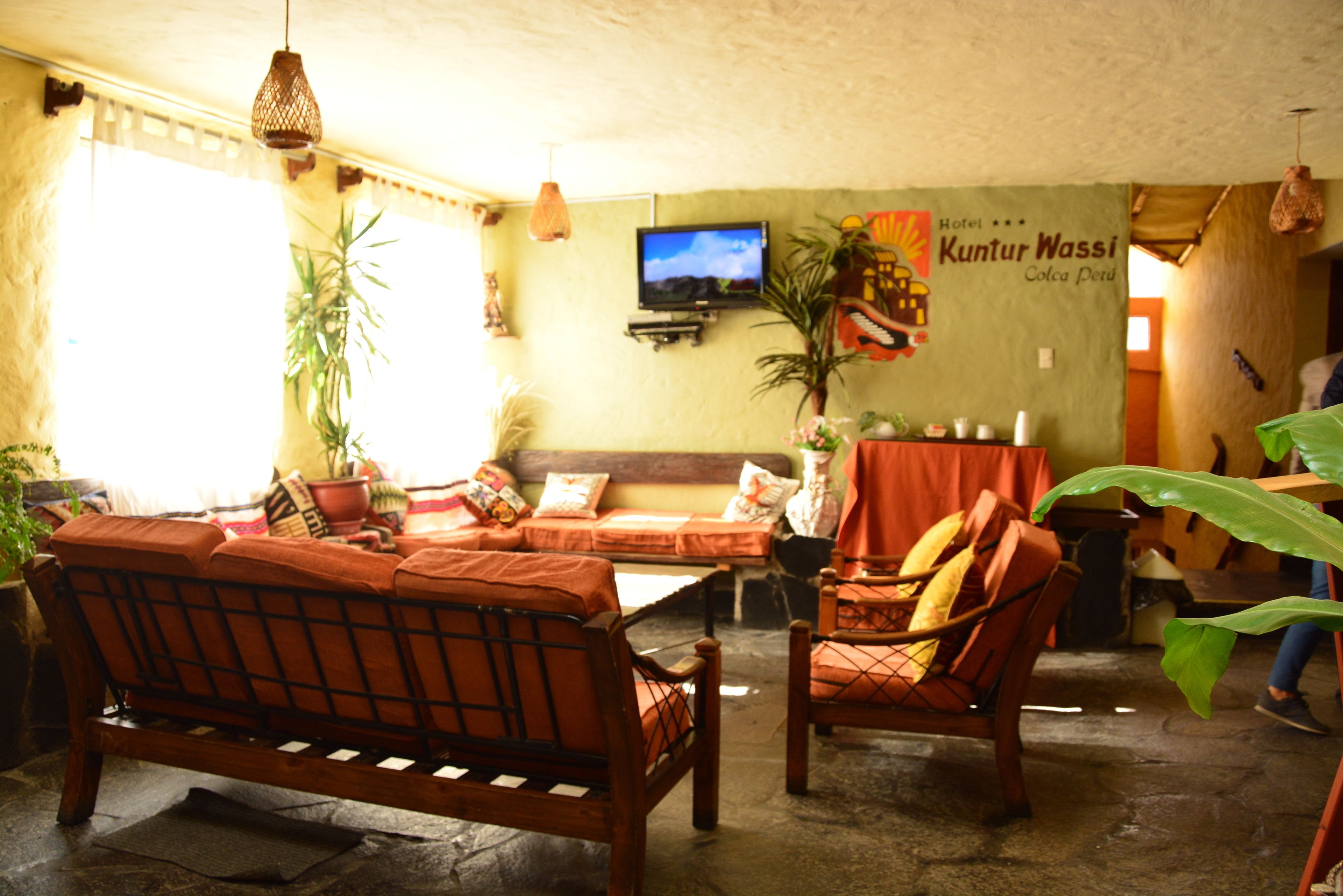 A cozy room with a sofa, chairs, a TV, and a sign for Hotel Kuntur Wassi.
