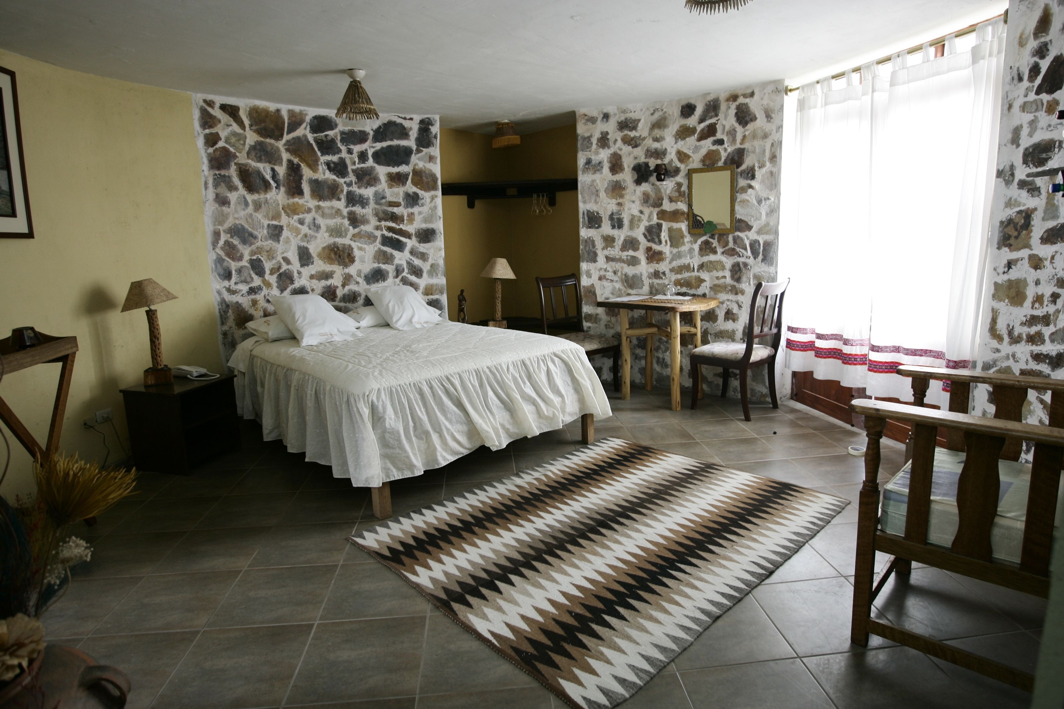 A bedroom with a bed, a small table, a chair, and a rug.