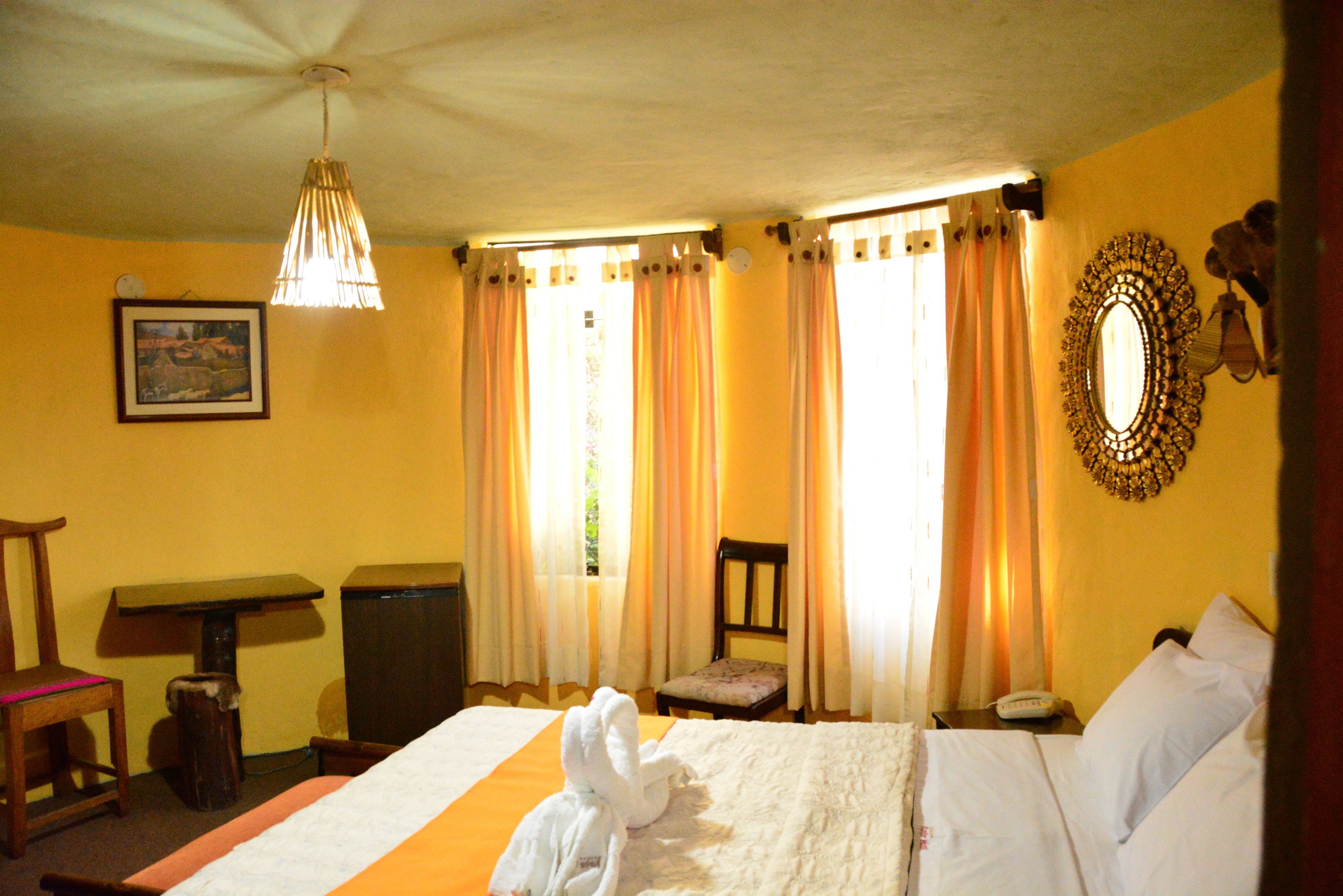 A hotel room with a bed, a chair, a desk, a mirror, and curtains.