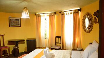 A hotel room with a bed, a chair, a desk, a mirror, and curtains.