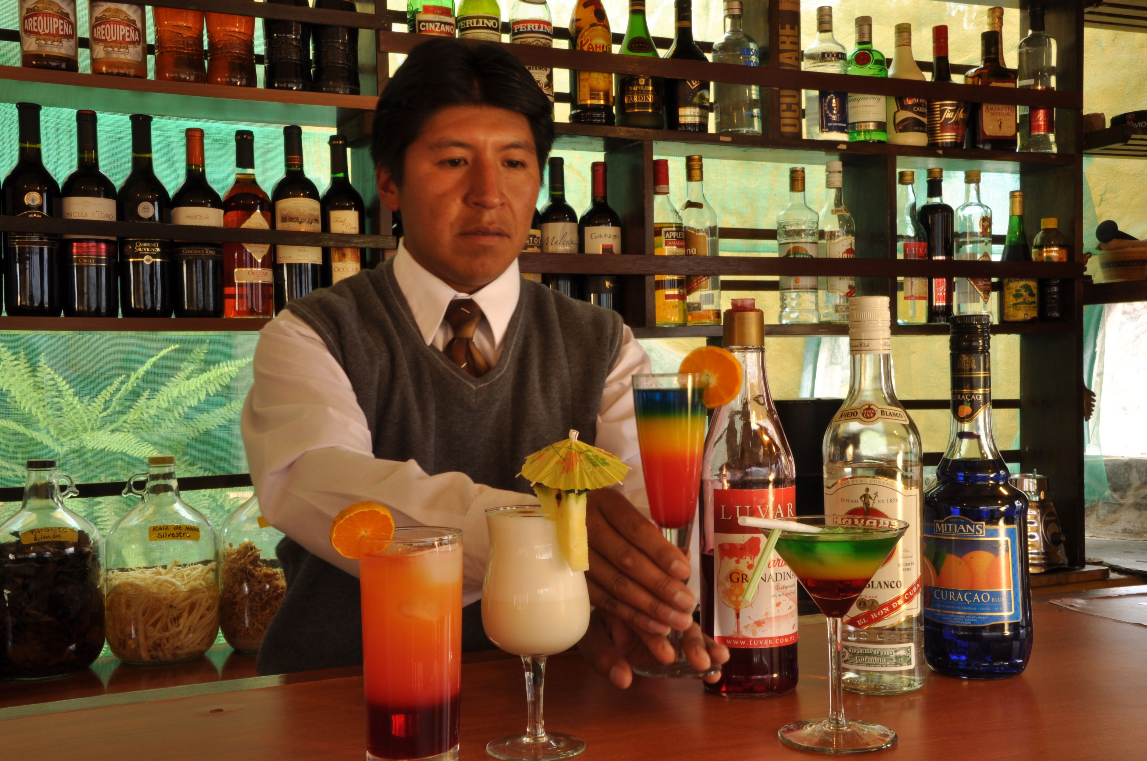 A bar with various bottles and a bartender preparing drinks.
