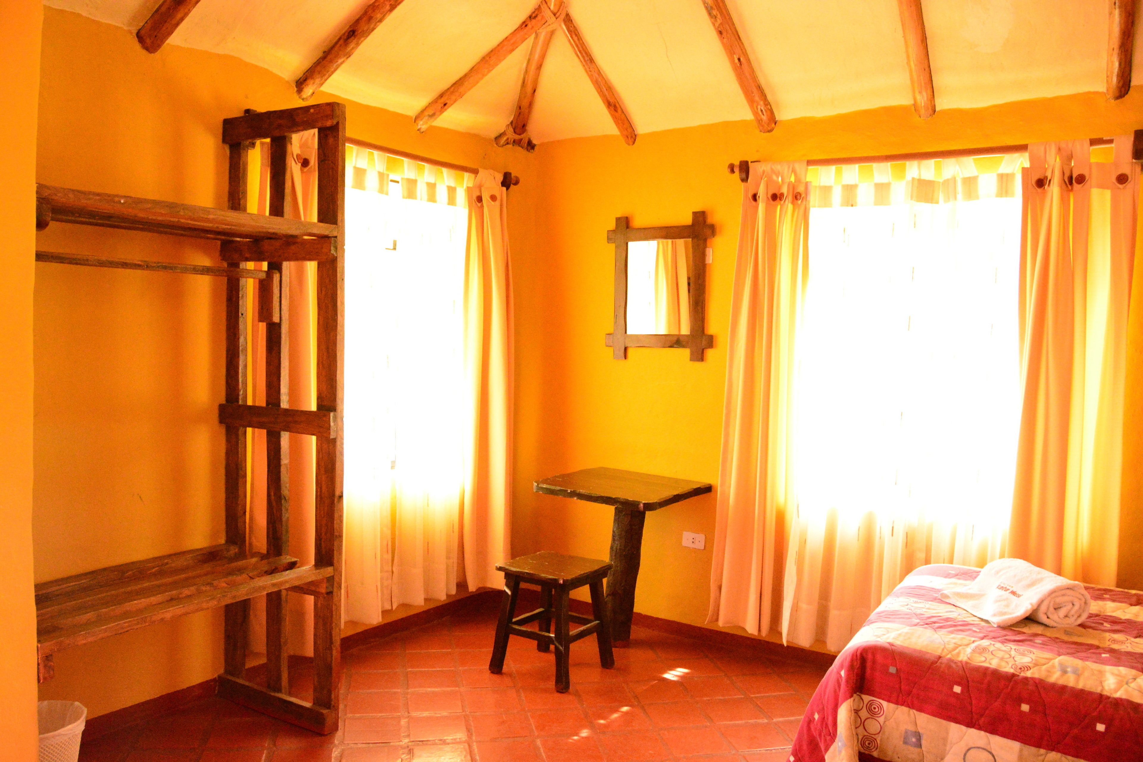 A room with a wooden bench, a small table, a bed with a quilt, and a window with curtains.