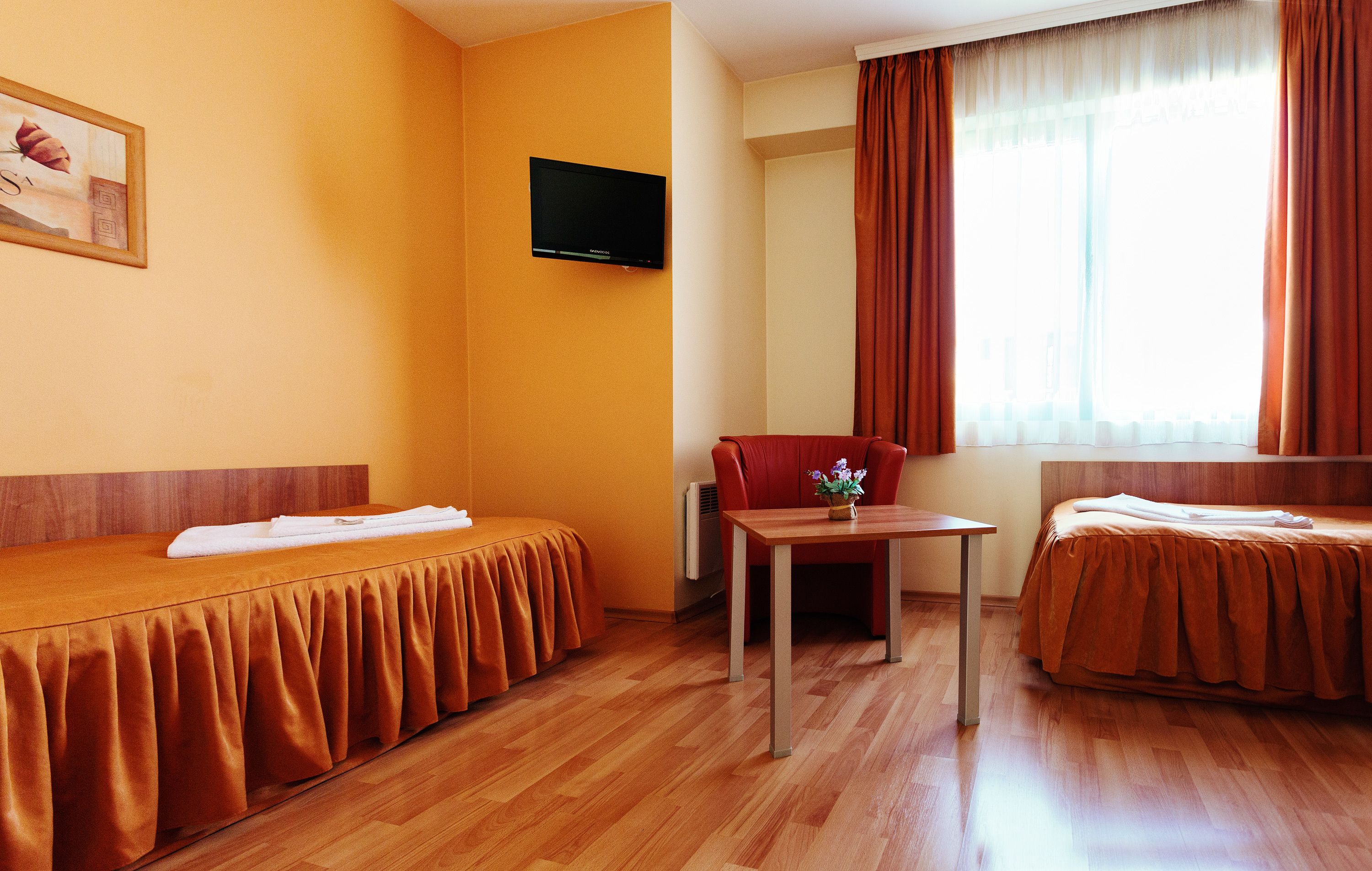 Habitación de hotel con dos camas, un televisor, una mesita con un jarrón y una ventana con cortinas.