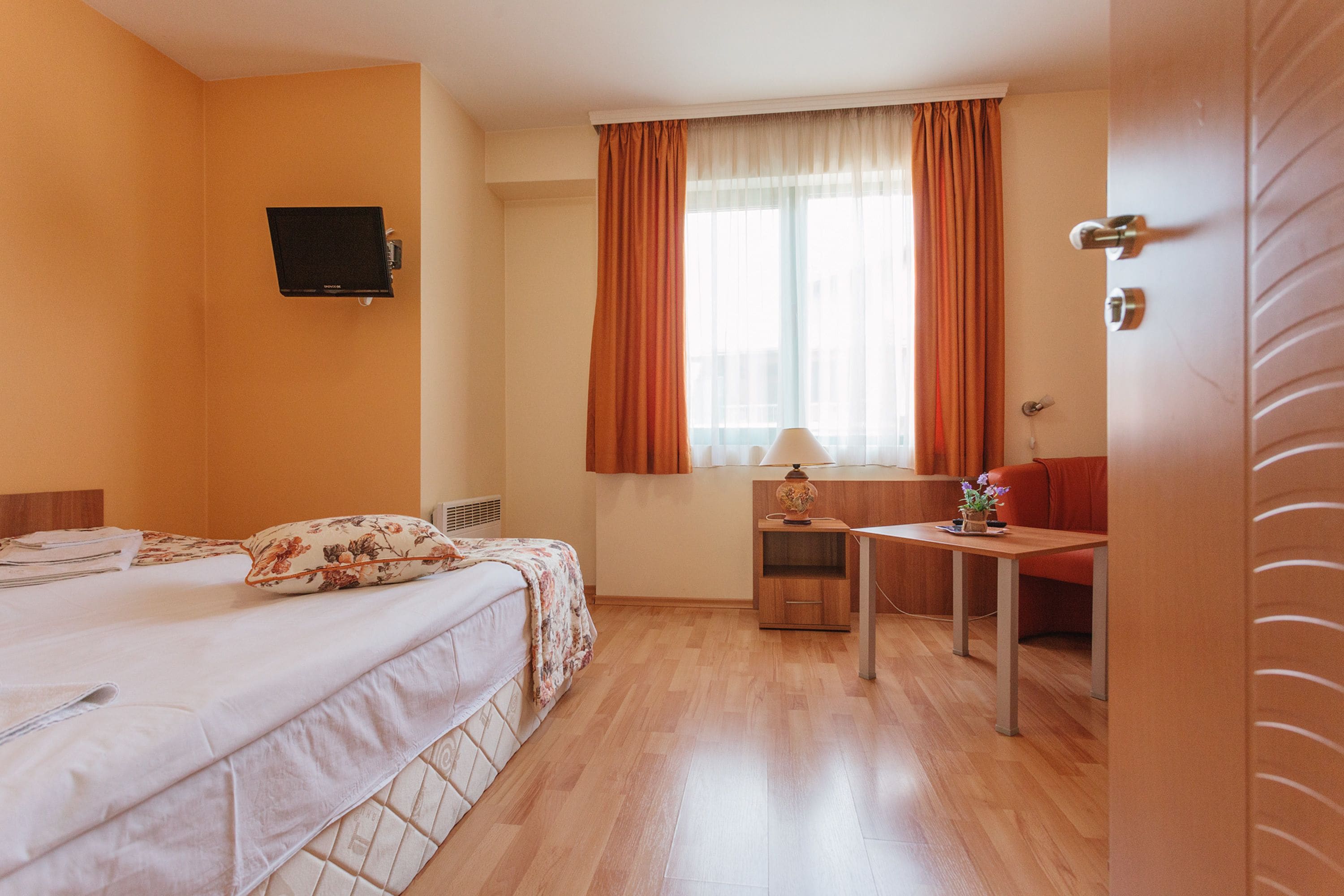 Hotellihuone, jossa on sänky, työpöytä, tuoli, televisio ja ikkuna, jossa on verhot.