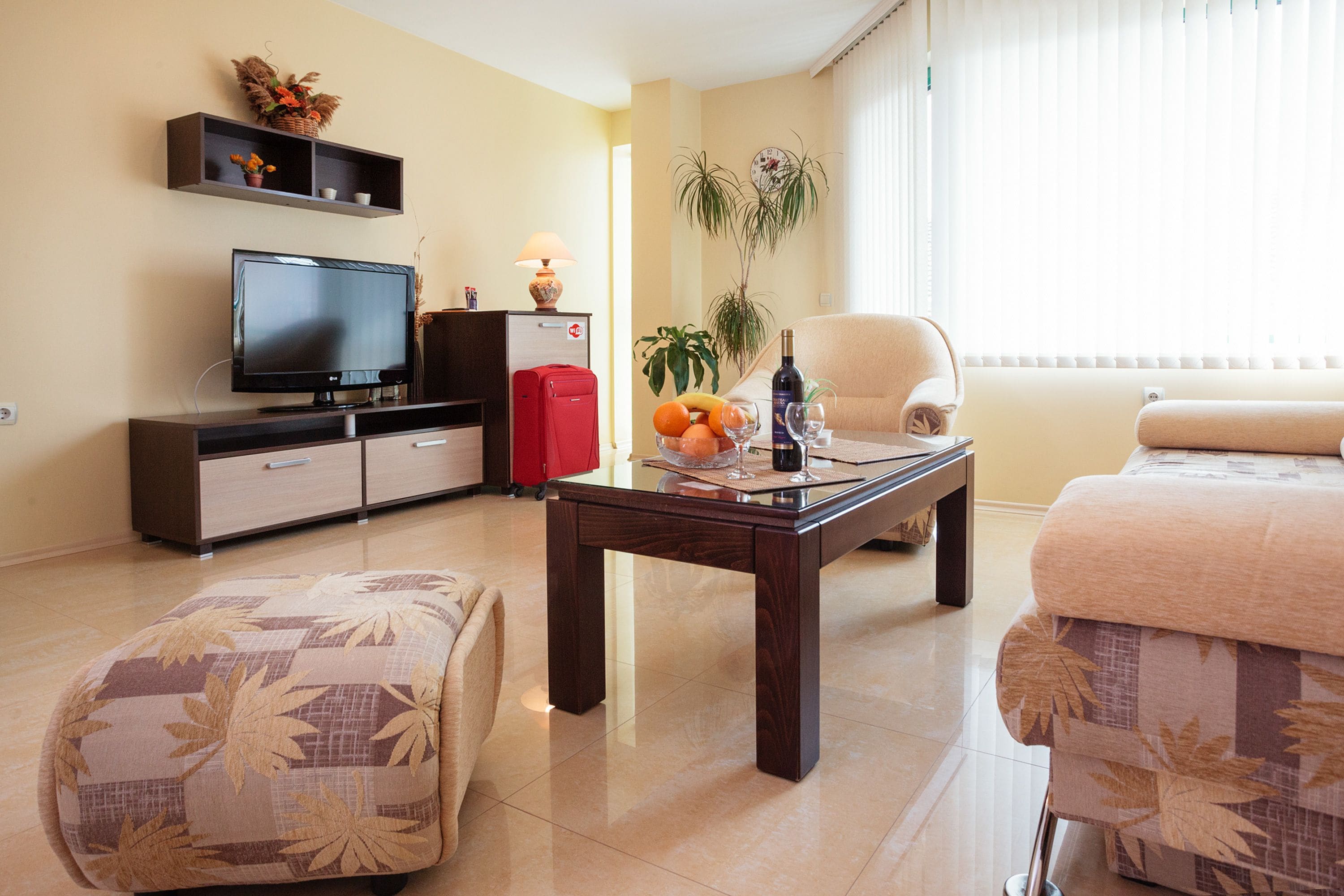 A living room with a TV, sofa, ottoman, and a coffee table with fruit and a bottle.