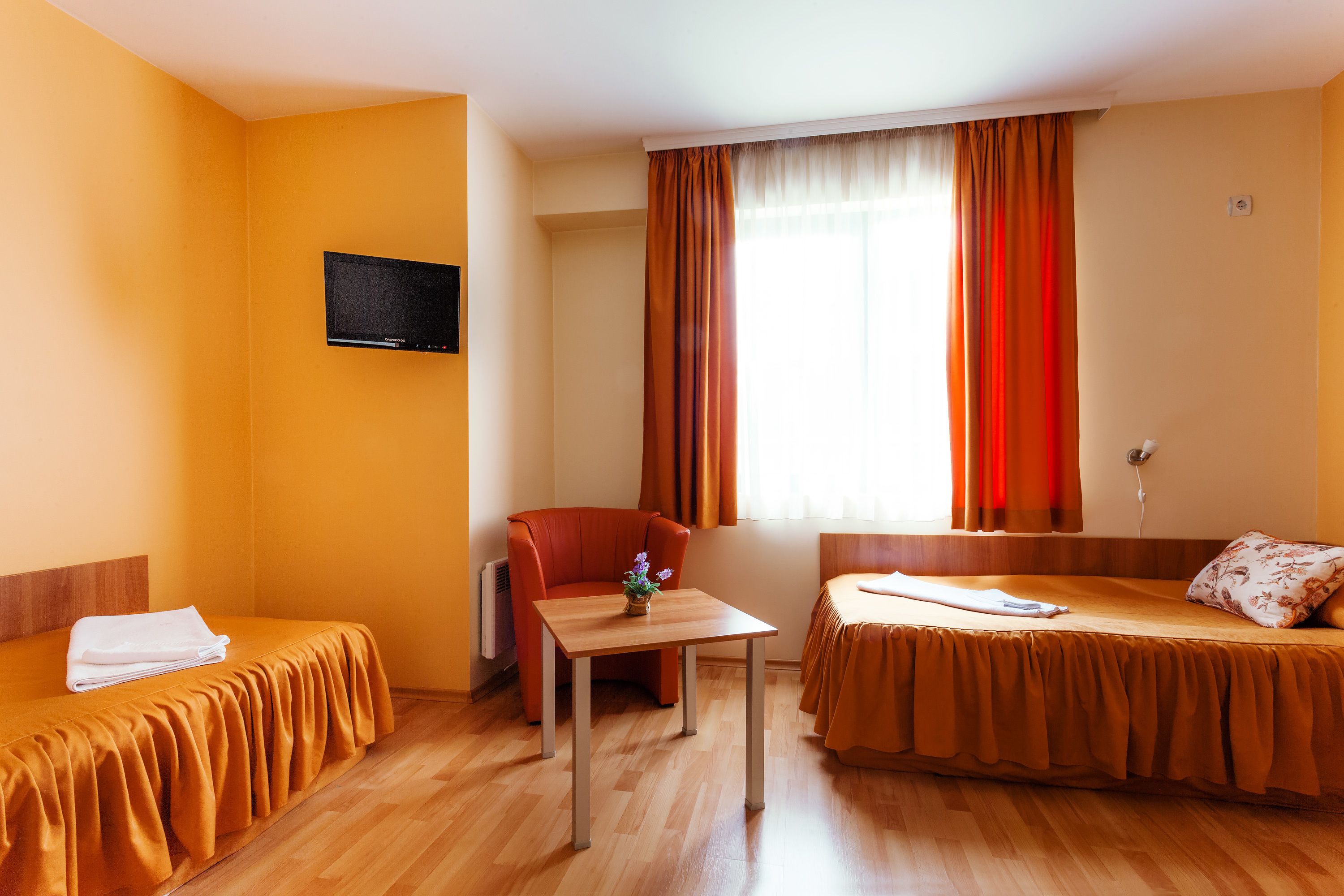A hotel room with two beds, a small table, a TV, and a window with curtains.