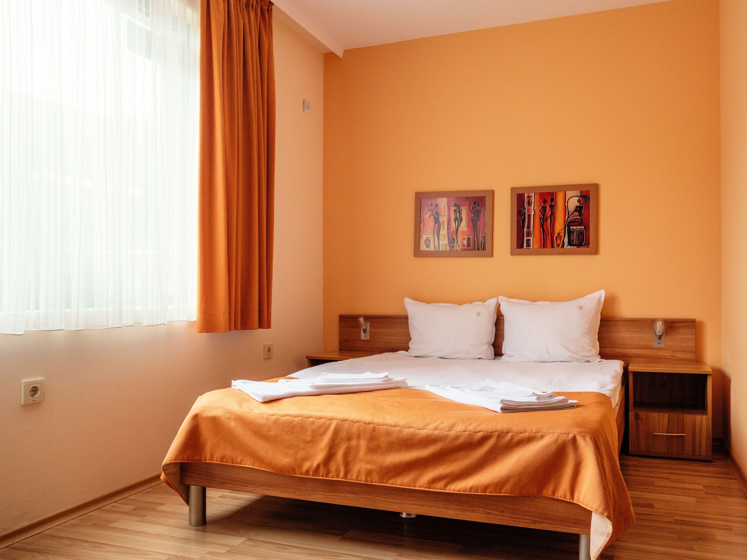 Ein Hotelzimmer mit einem Bett, zwei Kissen, einem hölzernen Kopfteil, einem Nachttisch und zwei Bildern an der Wand.