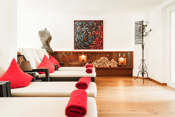 A spa room with multiple massage tables, red towels, a fireplace with logs, and a modern abstract painting.