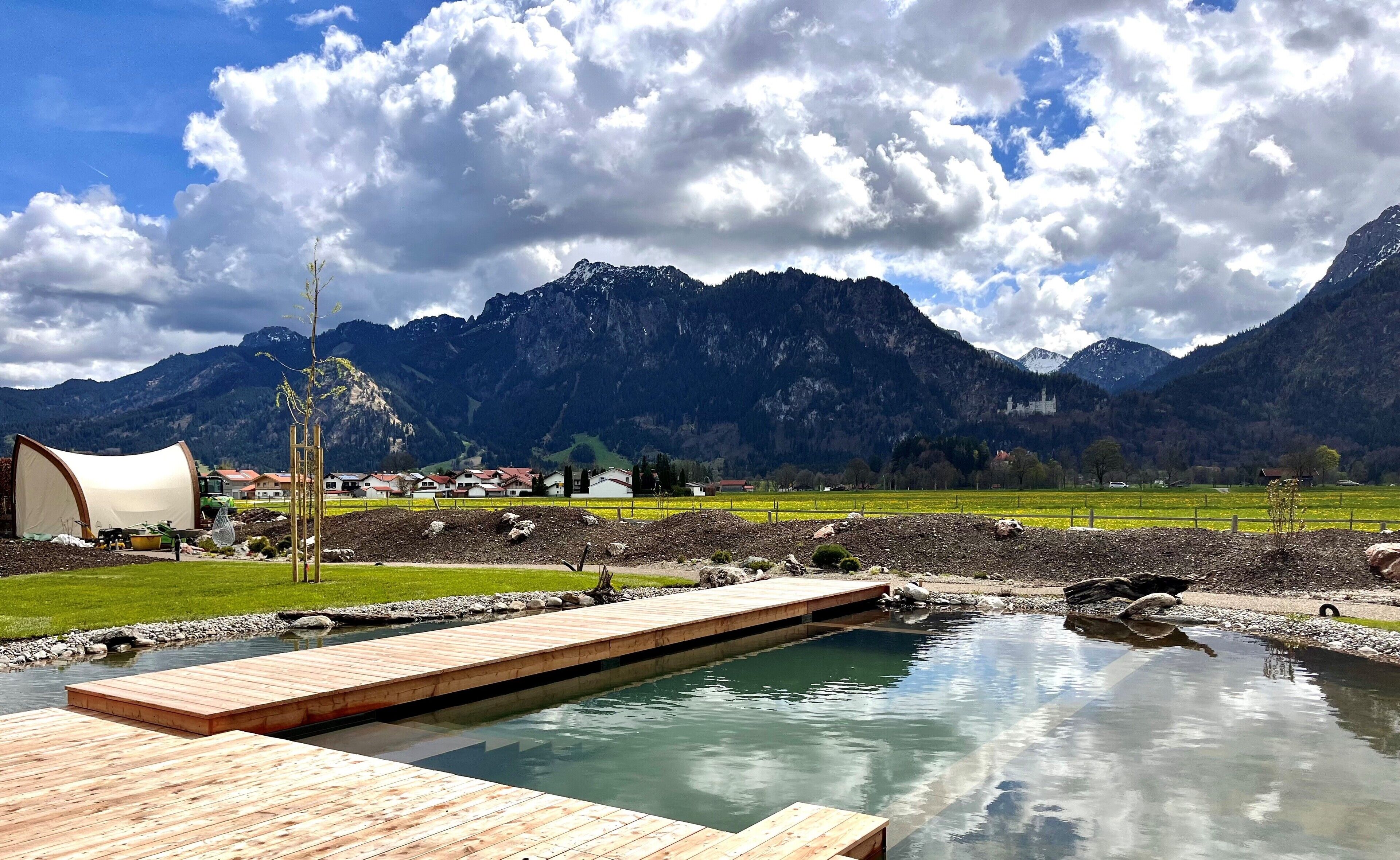 A wooden deck leading to a clear pool with a mountain backdrop.