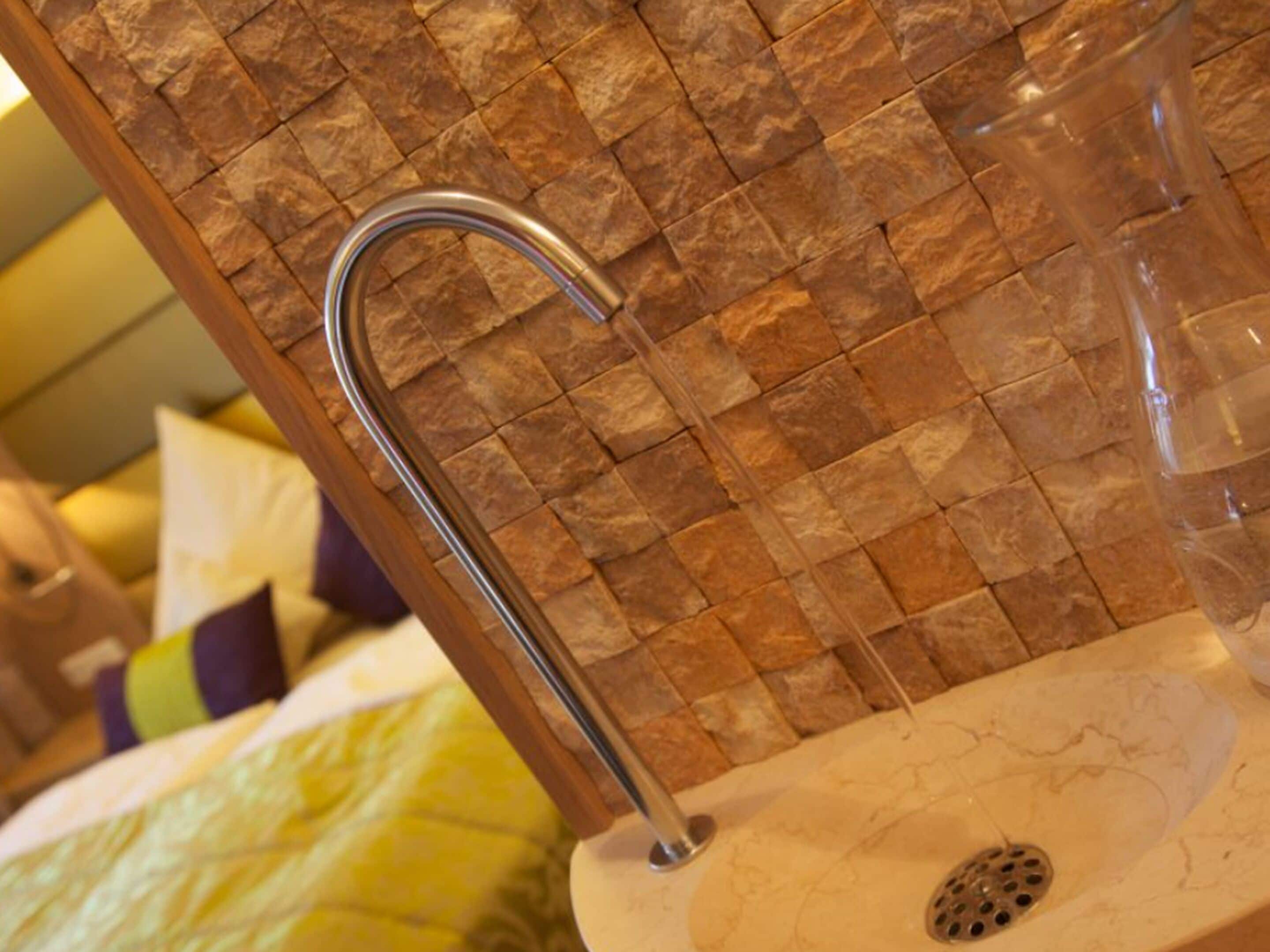 Un baño con pared de piedra, un lavabo y zona de ducha.