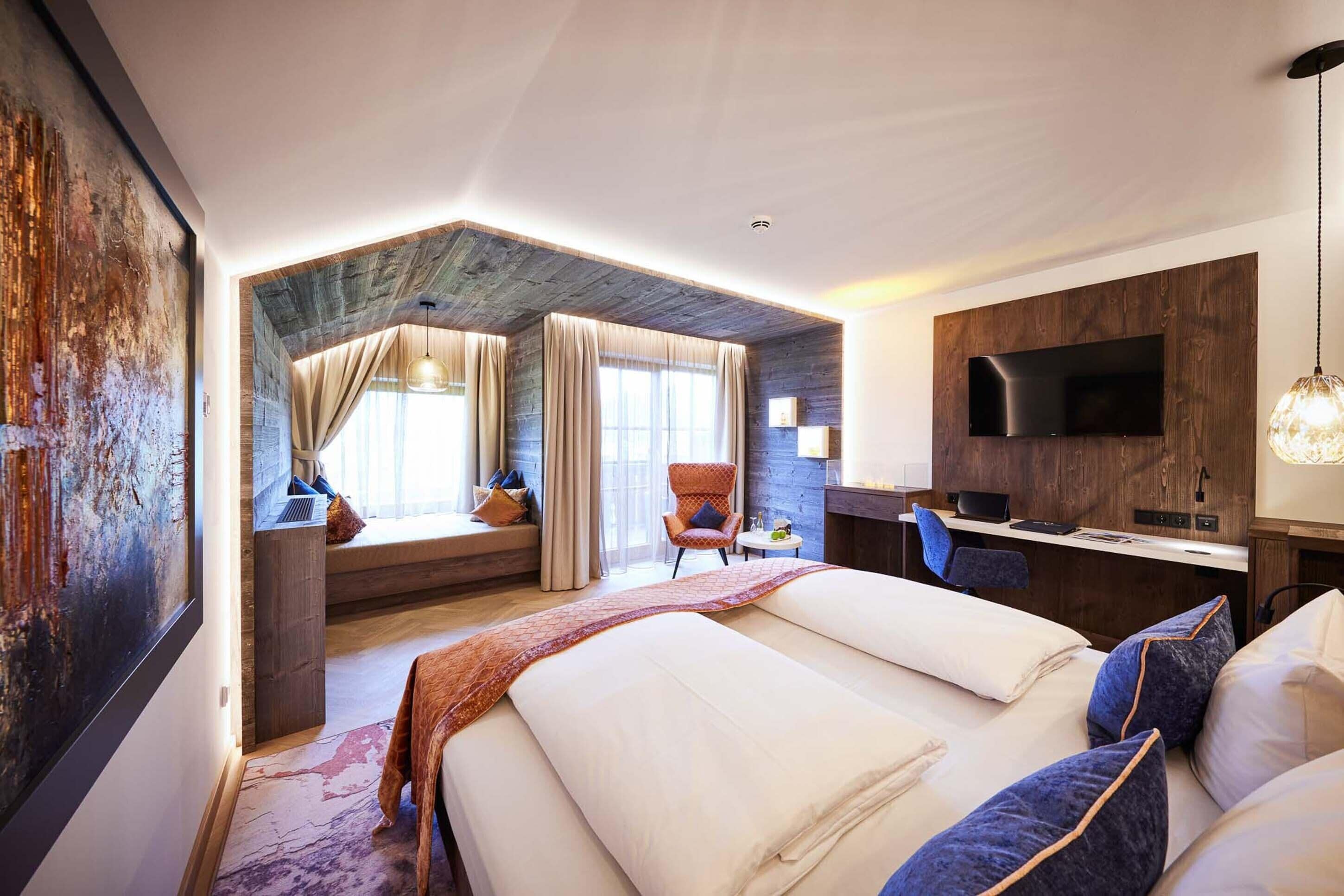 A modern hotel room with a large bed, a desk, a TV, and a view of the outdoors.