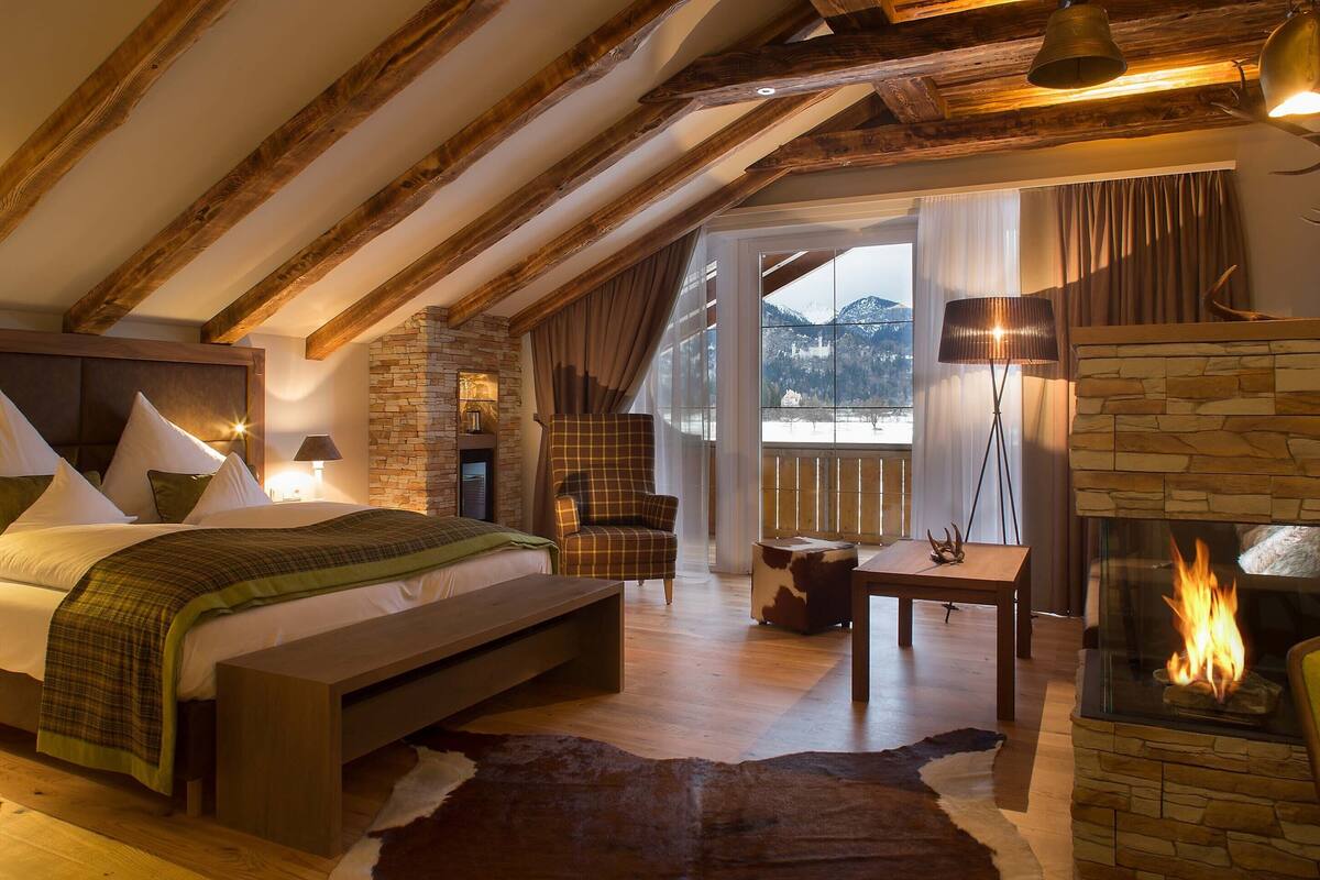 Une chambre spacieuse avec un grand lit, une cheminée en pierre et une vue sur les montagnes par une grande fenêtre.
