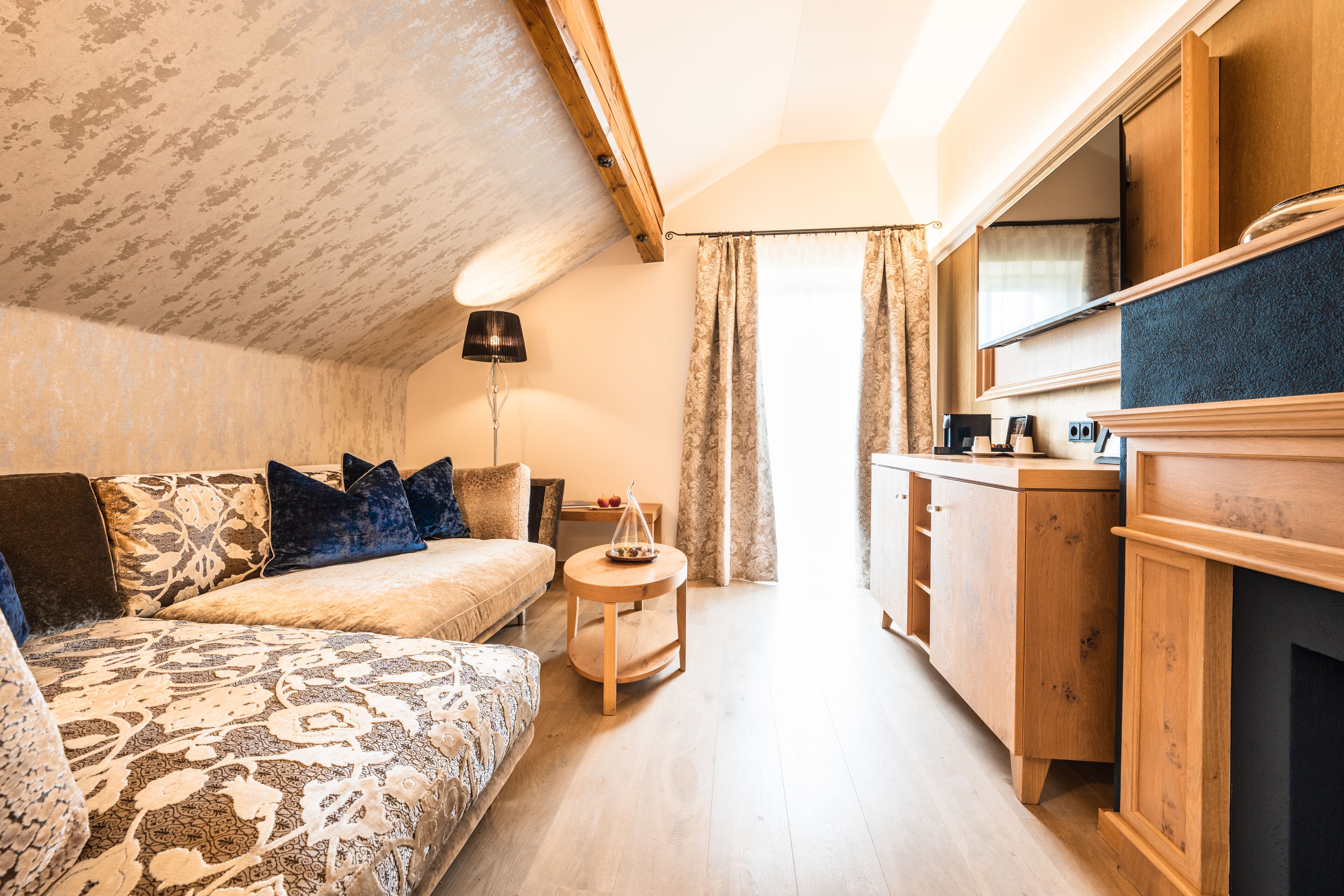 A cozy bedroom with a bed, bedside table, and a small round table with a lamp.