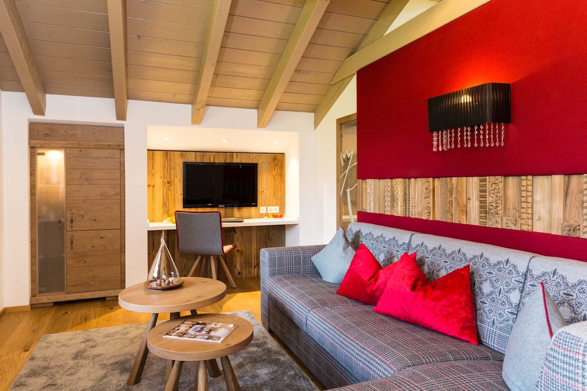 Un salon moderne avec un plafond en bois, un mur d’accent rouge, un canapé agrémenté de coussins à motifs et un coin repas équipé d’un téléviseur.