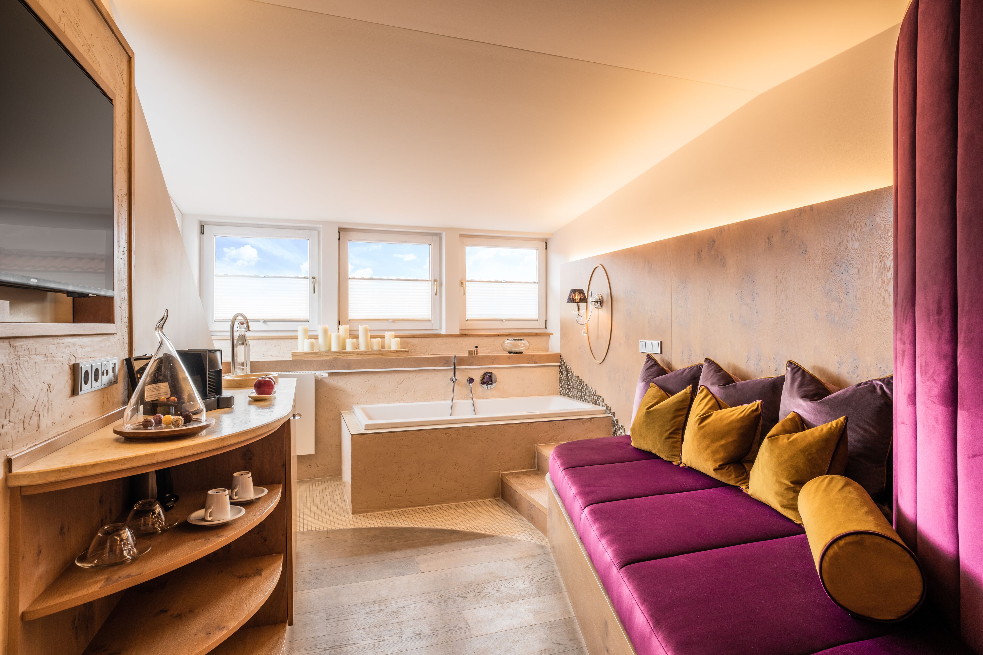 A modern bathroom with a bathtub, vanity, and a purple sofa with cushions.
