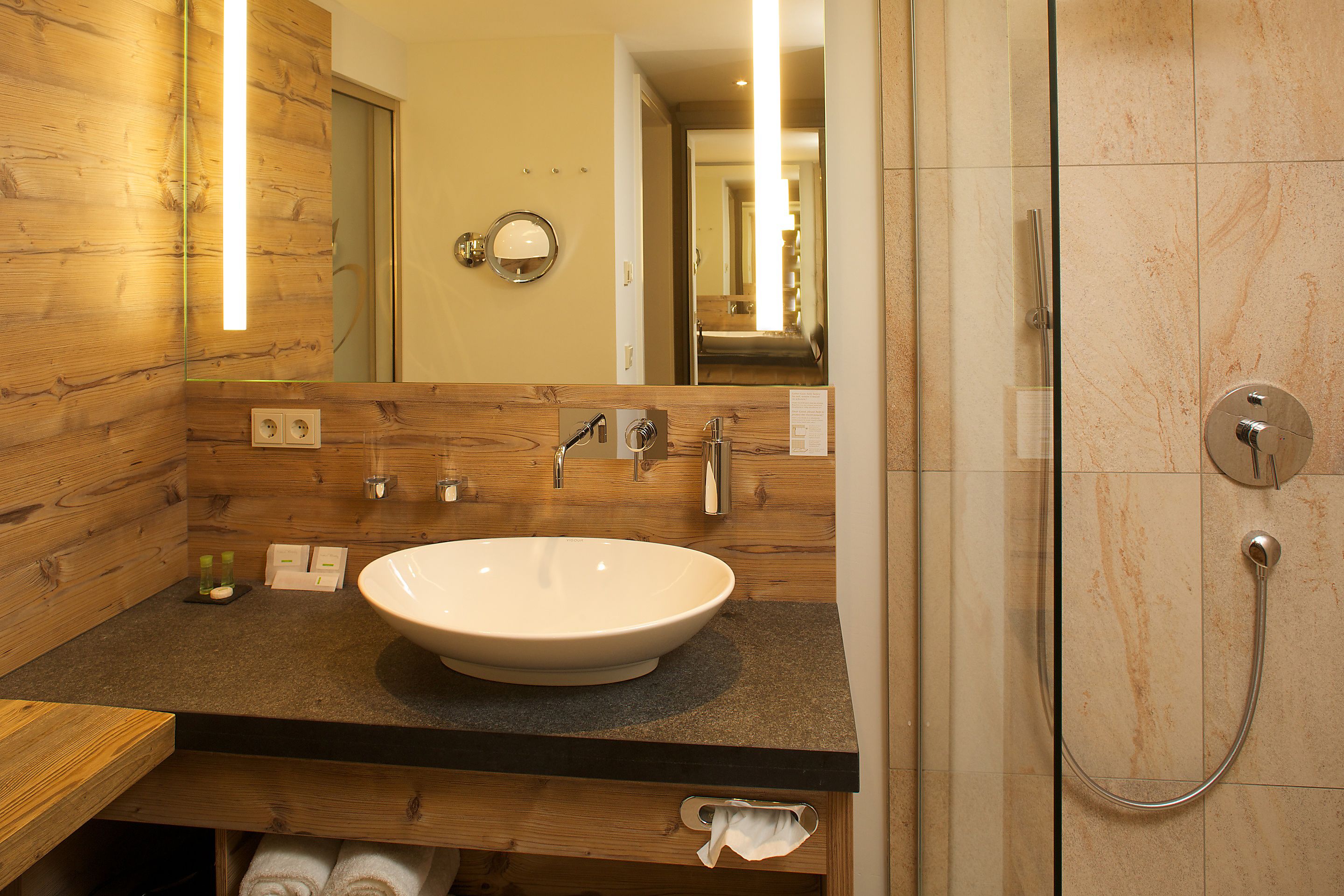 A modern bathroom with a wooden vanity, a large sink, and a glass-enclosed shower.