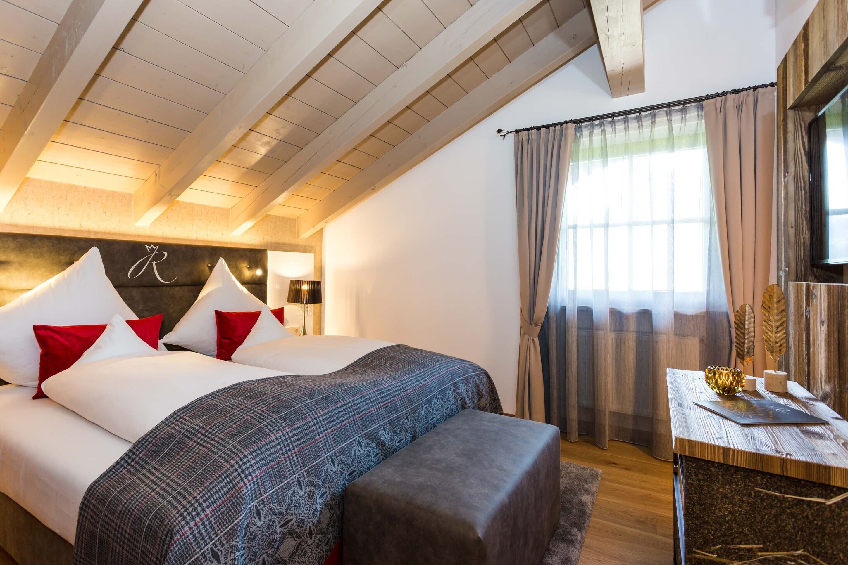 A hotel room with a large bed, a desk with a lamp, and a window with curtains.