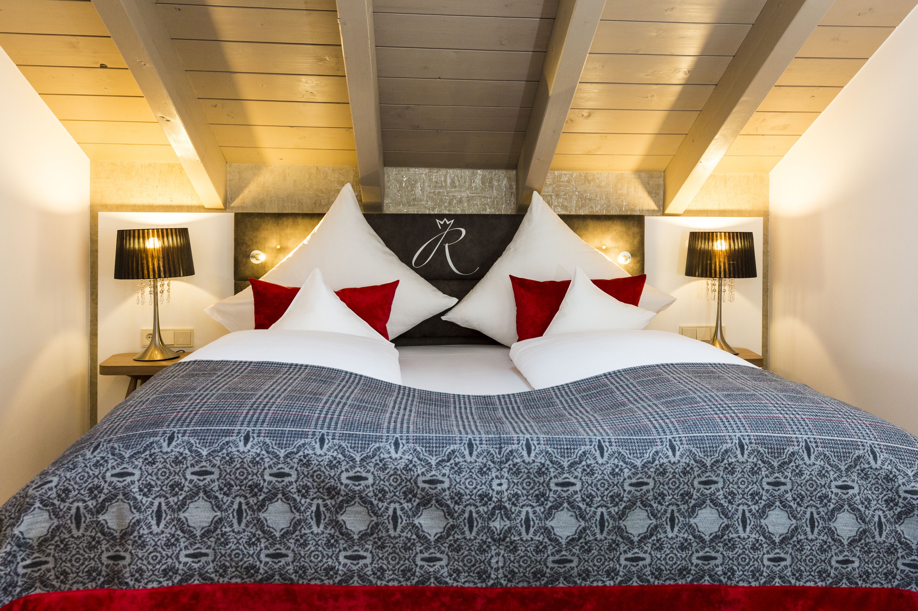 A bedroom with a bed, two bedside tables, and a headboard with a letter 'R'.