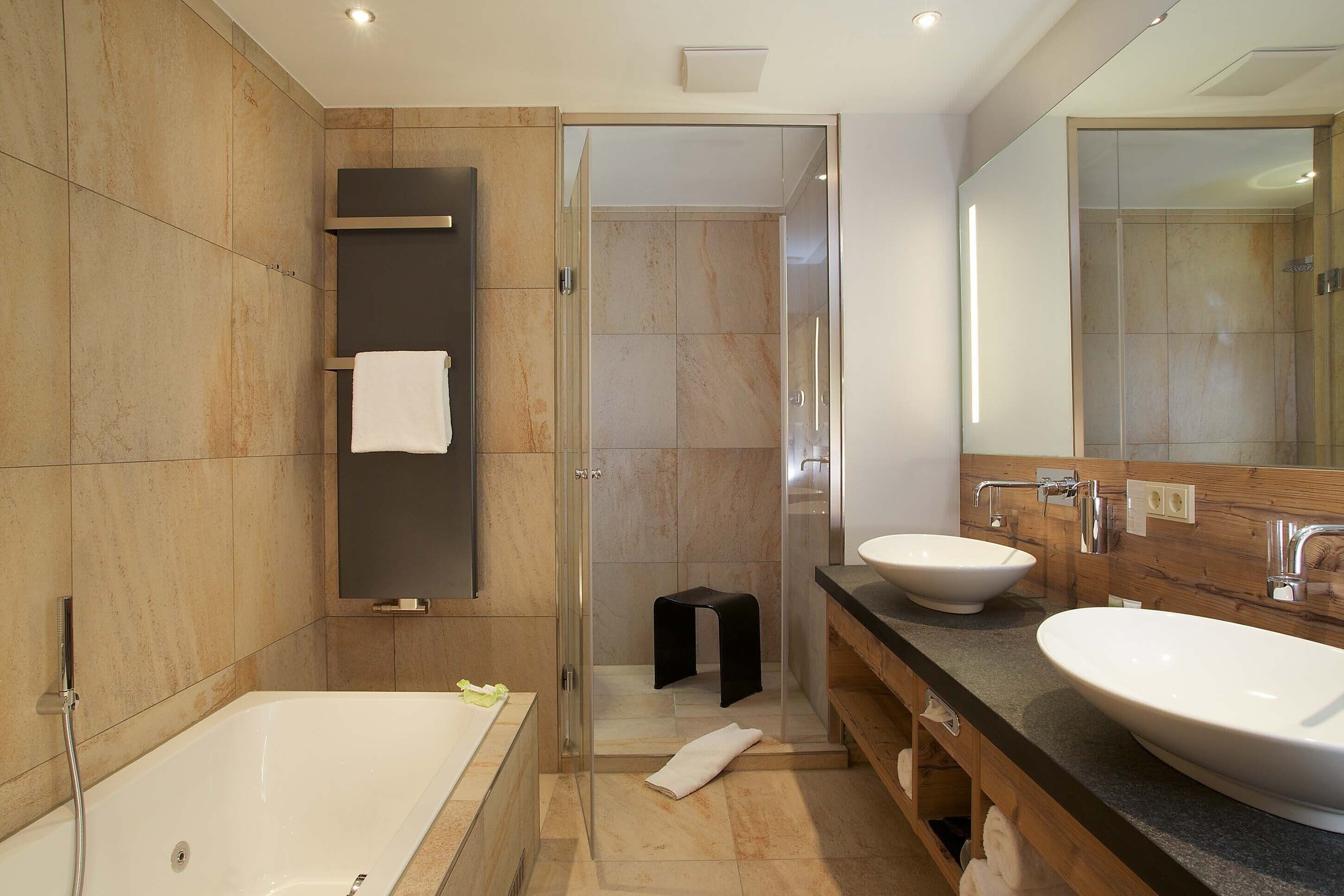 A modern bathroom with a bathtub, two sinks, a glass shower enclosure, and a wooden vanity.
