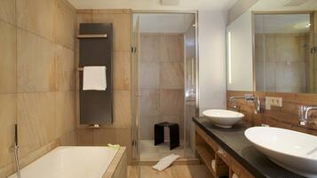 A modern bathroom with a bathtub, two sinks, a glass shower enclosure, and a wooden vanity.