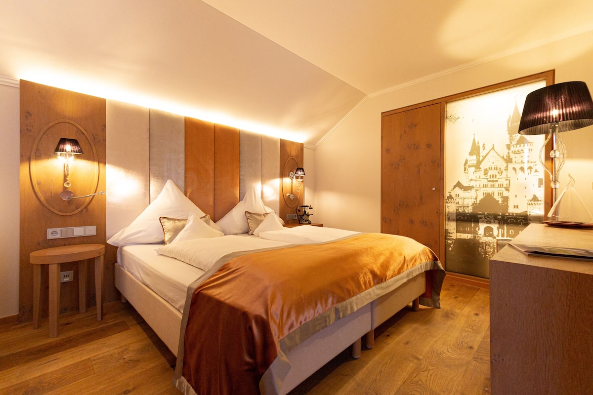 Une chambre à coucher avec un grand lit, deux tables de chevet et une petite table de nuit. Chaque table de chevet est équipée d’une lampe fixée au mur.