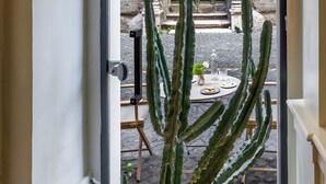 A doorway leading to an outdoor area with a stone building, a green door, and a cactus plant. - Nerva Boutique Hotel (Rome)