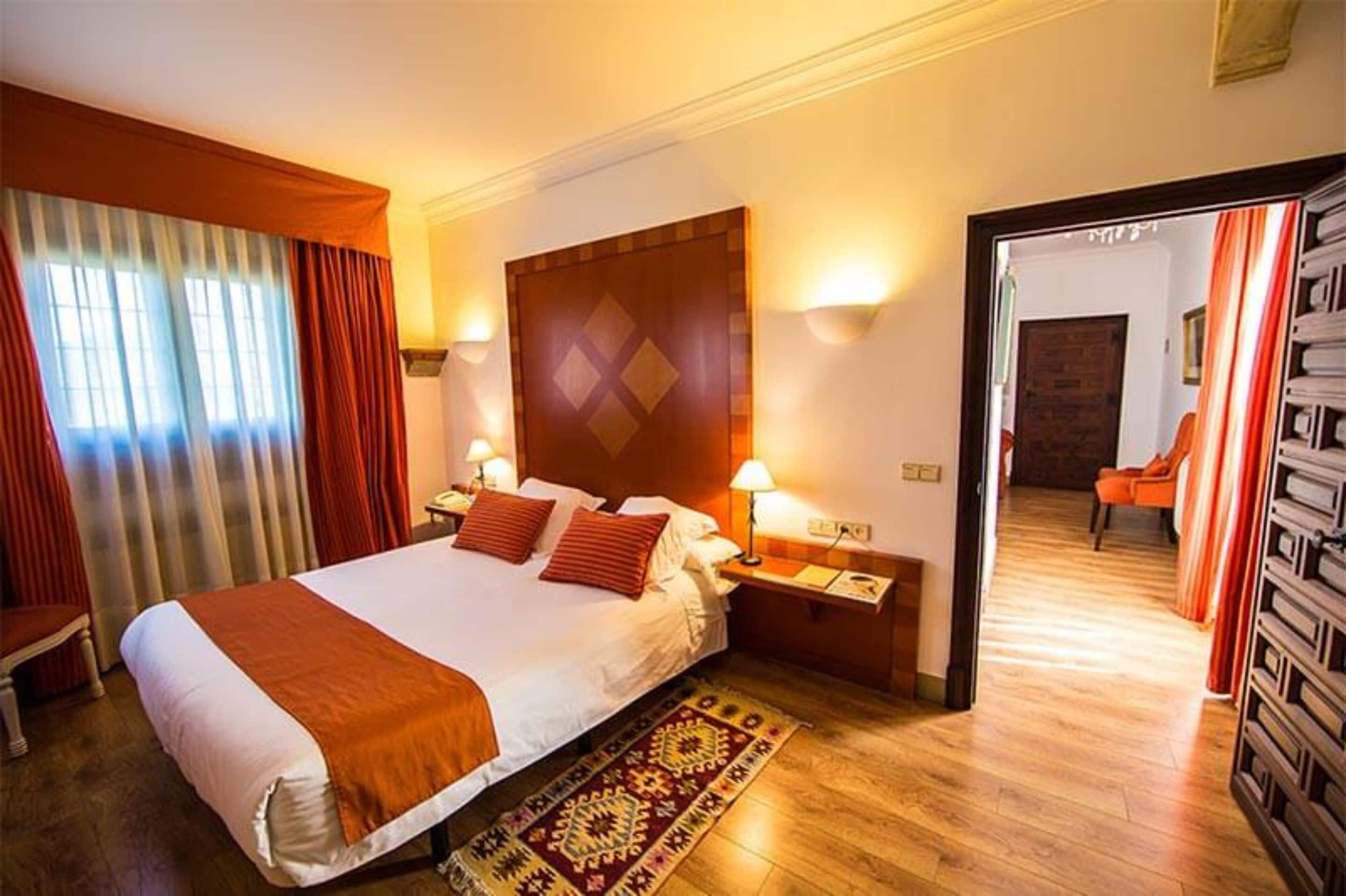 Une chambre d’hôtel avec un grand lit, deux tables de chevet avec des lampes, un tapis à motifs et un plancher en bois.